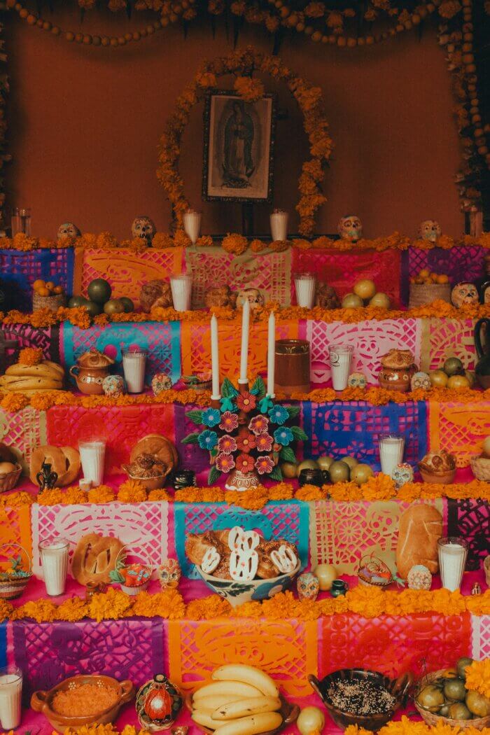 Tradiční mexický oltář ofrenda k Día de los Muertos, ozdobený květy cempasúchil, papel picado, svíčkami, ovocem a chlebem mrtvých.
