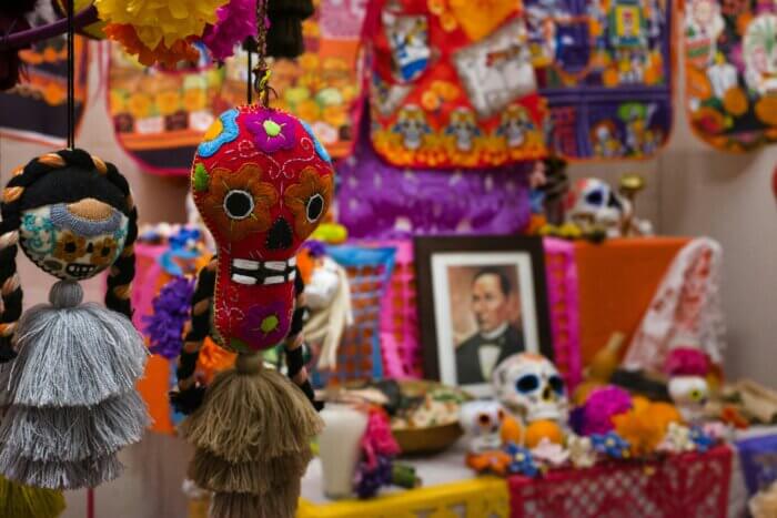 Ručně vyšívané ozdoby a barevné lebky na mexickém oltáři ofrenda během svátku Día de los Muertos.