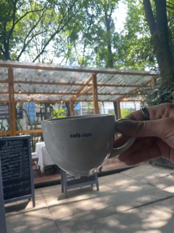 Ruka držící bílý hrnek s nápisem Café Rico v kavárně v čtvrti Condesa, Mexico City.