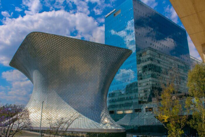 Futuristická budova Museo Soumaya v Mexico City s lesklou kovovou fasádou a skleněným mrakodrapem v pozadí.