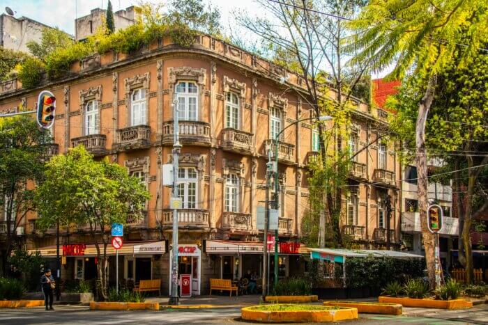 Historická budova s kavárnami a restaurací Marcello v Colonia Roma, Mexico City, s typickou secesní fasádou a zelení kolem.