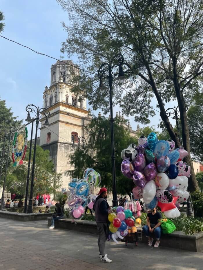 Kostel San Juan Bautista v Coyoacánu v Mexico City s prodejci balónků a lidmi na rušném náměstí.