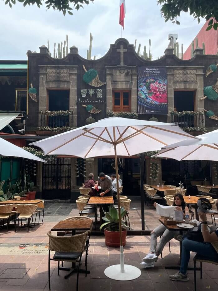 Pohled na restauraci Los Danzantes v Coyoacánu, Mexico City, s krásnou kamennou fasádou a zahrádkou se slunečníky.
