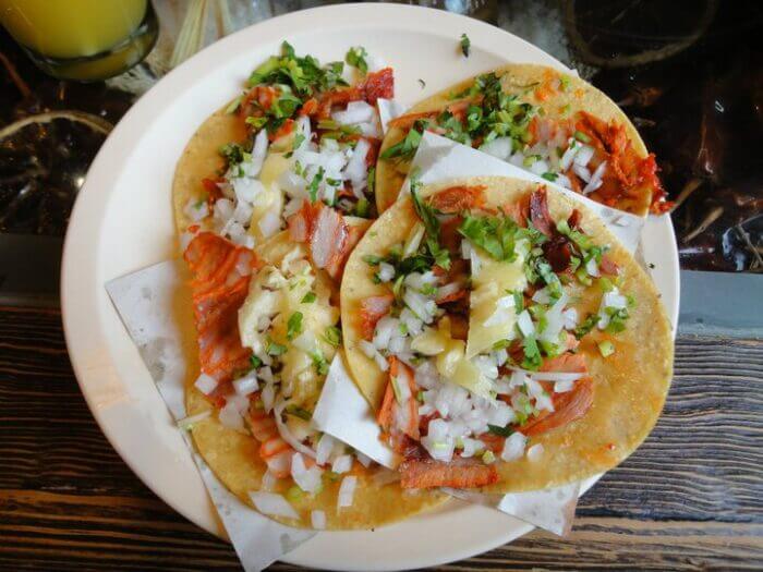 Tacos al pastor s ananasem a cibulí na bílém talíři – klasika z Mexico City.
