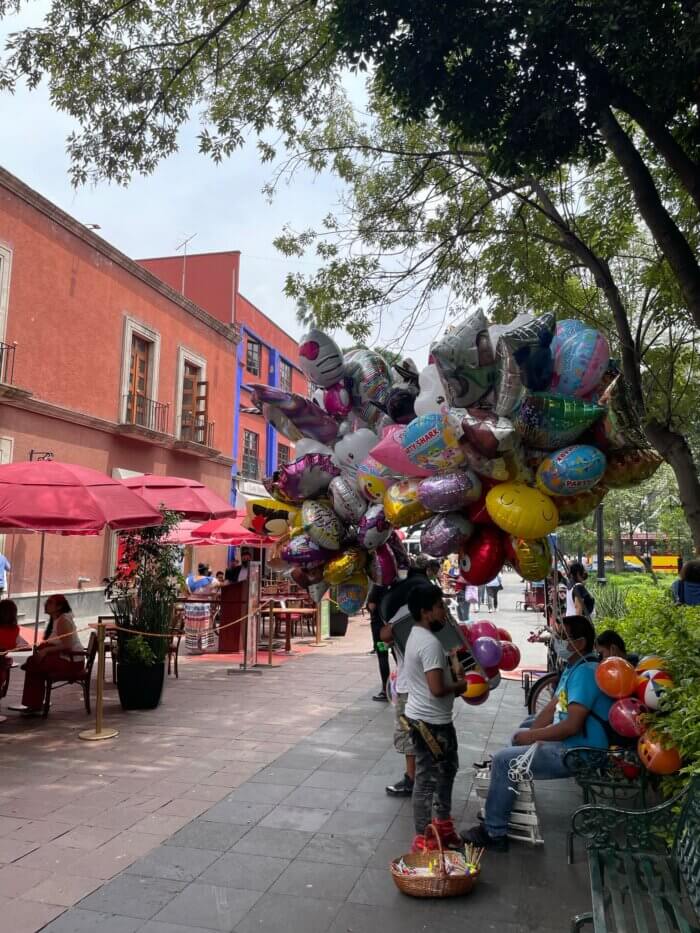 Koloniální domy a prodejci balónků na malebném náměstíčku ve čtvrti San Ángel v Mexico City.