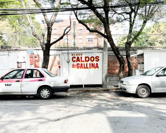 Auto taxi de sitio a pouliční stánek s nápisem Caldos de Gallina – typický pohled na ulici Mexico City.