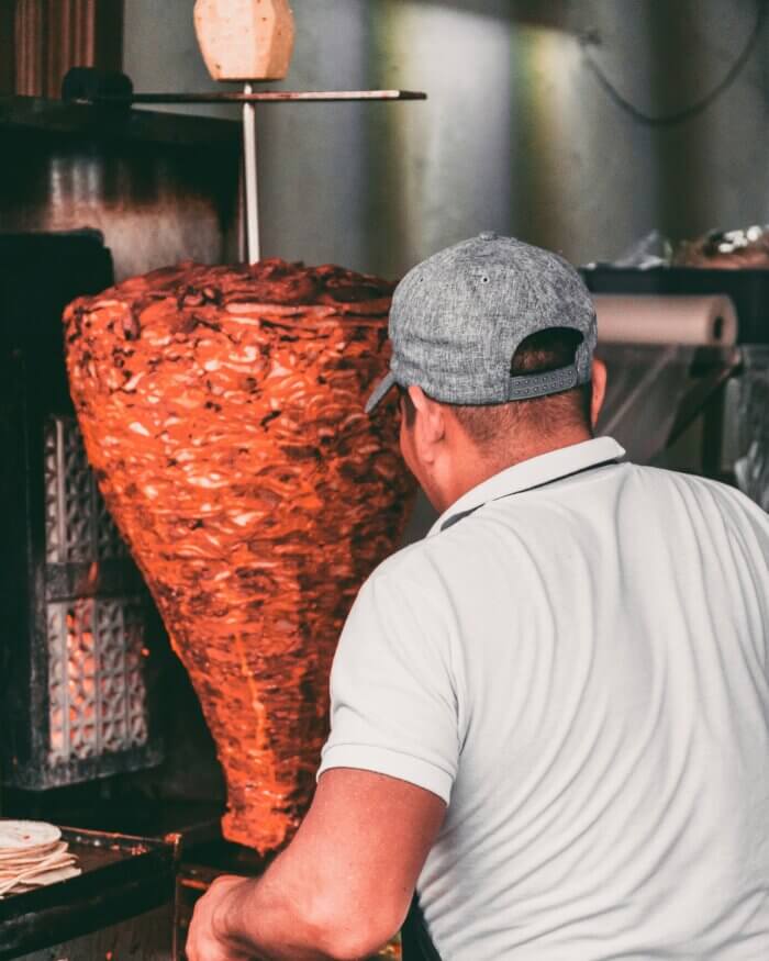 Trompo s marinovaným masem na tacos al pastor, připravované na vertikálním rožni v mexickém stánku.