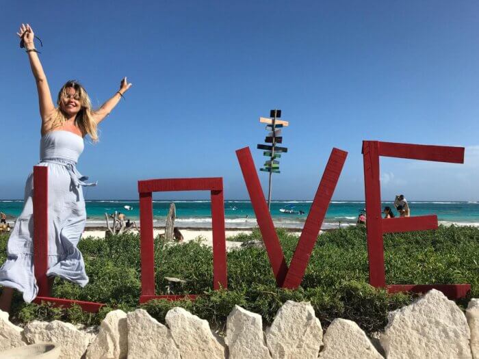 Žena stojící u nápisu LOVE na pláži Playa Paraíso v Tulum v Mexiku s tyrkysovým Karibikem v pozadí