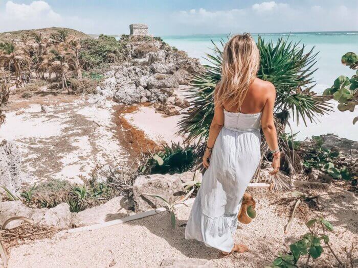 Žena stojící na útesu u pláže v Tulum, v pozadí jsou mayské ruiny Tulum